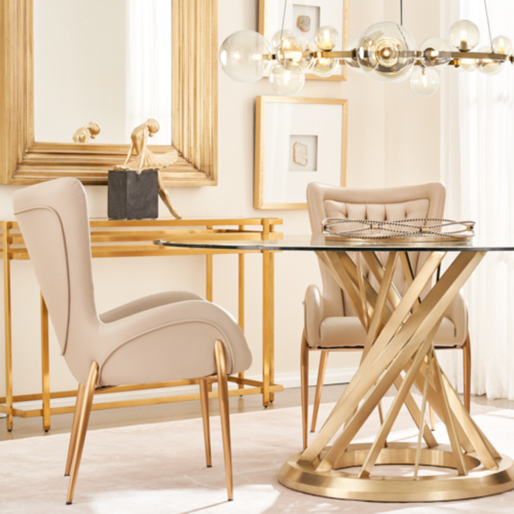 A contemporary dining chair draped in sand beige-colored vegan leather with a channel-tufted curved backrest, supported by four brushed golden-colored legs.