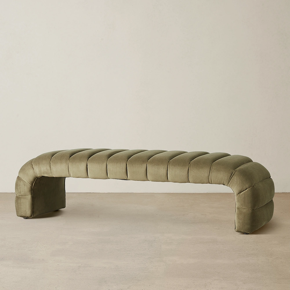 Olive Green-colored velvet ottoman with curved bench-like design and vertical tufts.